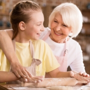 Happy grandmother and grandchild kneading dough on kitchen table