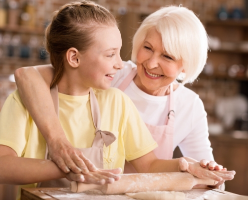 Happy grandmother and grandchild kneading dough on kitchen table